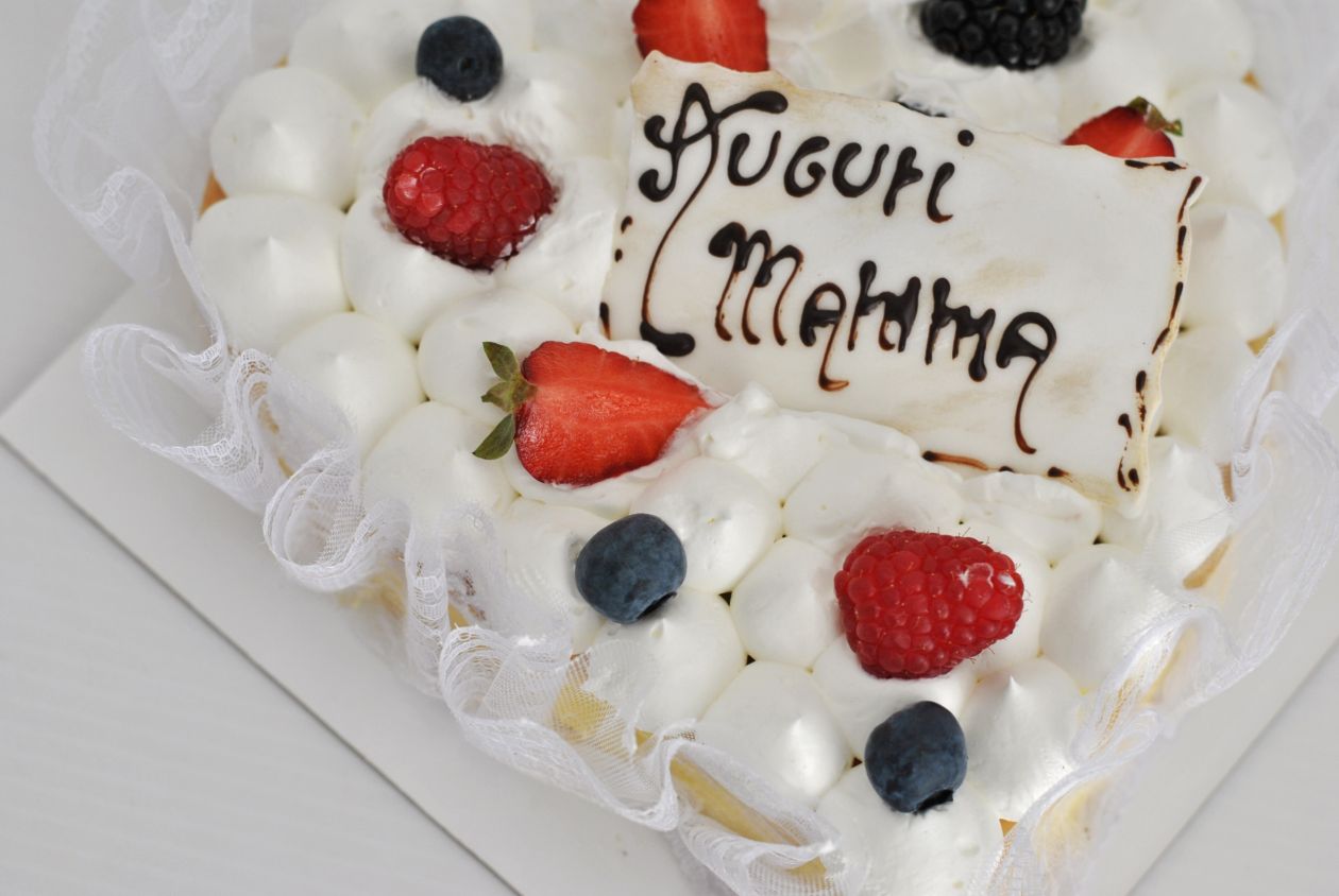 Torta alla crema a forma di cuore con la scritta Auguri Mamma, decorata con panna, fragole e mirtilli